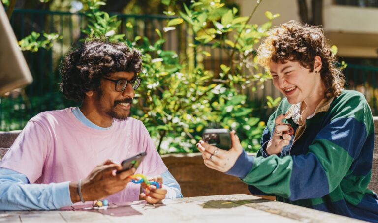 Two autistic friends sitting outside using stim toys and laughing at their phones